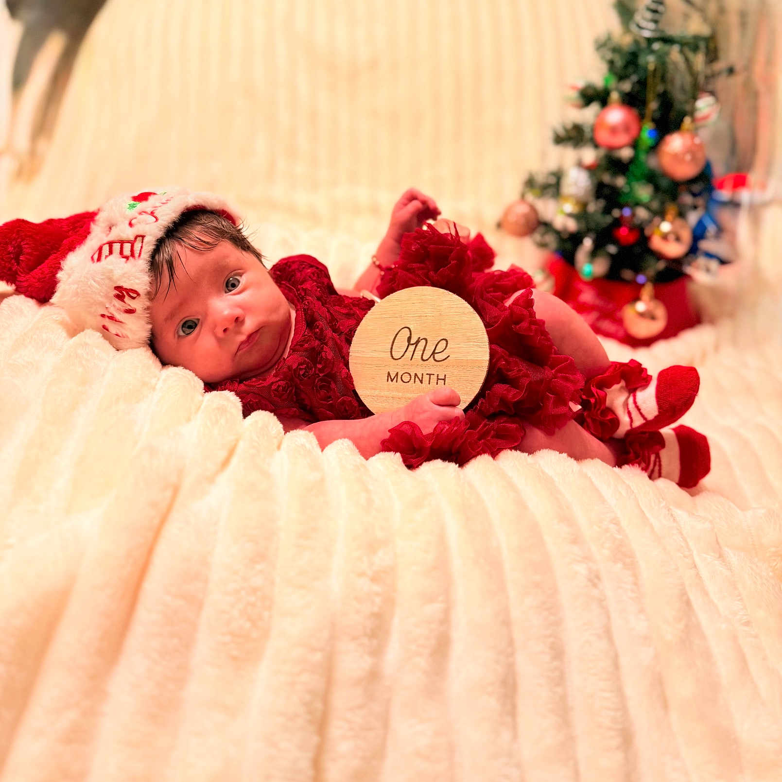 Meara is registered to the contest to win money with this photo: baby, blanket, celebration, christmas, cozy, cute, decorations, festive, hat, holiday, indoor, infant, lying_down, ornaments, portrait, red_clothing, socks, soft_texture, tree, wooden_sign