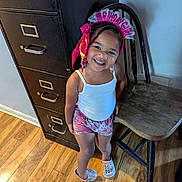 Anaya is registered to the contest to win money with this photo: child, toddler, birthday, tiara, smiling, portrait, standing, indoors, colorful_clothing, bow, tank_top, shorts, sneakers, filing_cabinet, folding_table, wood_floor, home, happy, girl, celebration