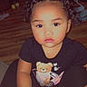 child, toddler, baby, portrait, sitting, indoors, curly_hair, pigtails, serious_expression, face, eyes, black_shirt, teddy_bear, clothing, wooden_floor, furniture, home, chair, emoji, photography