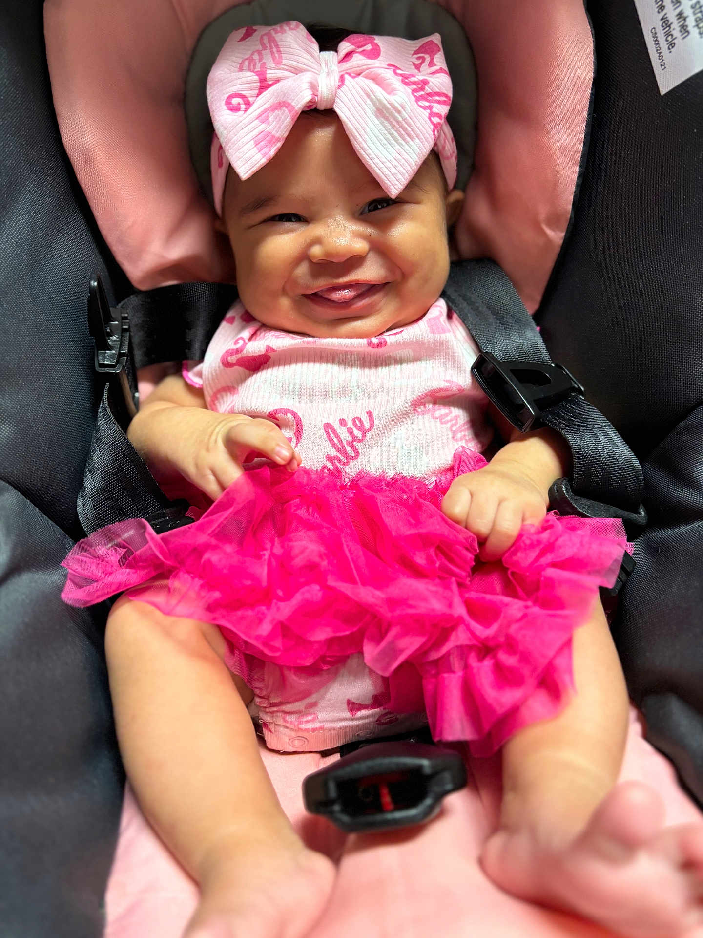 Azalea is registered to the contest to win money with this photo: baby, infant, child, car_seat, pink_bow, pink_dress, smiling, happy, cute, clothing, seatbelt, sitting, portrait, indoors, baby_girl, fabric, headband, human, skin, closeup