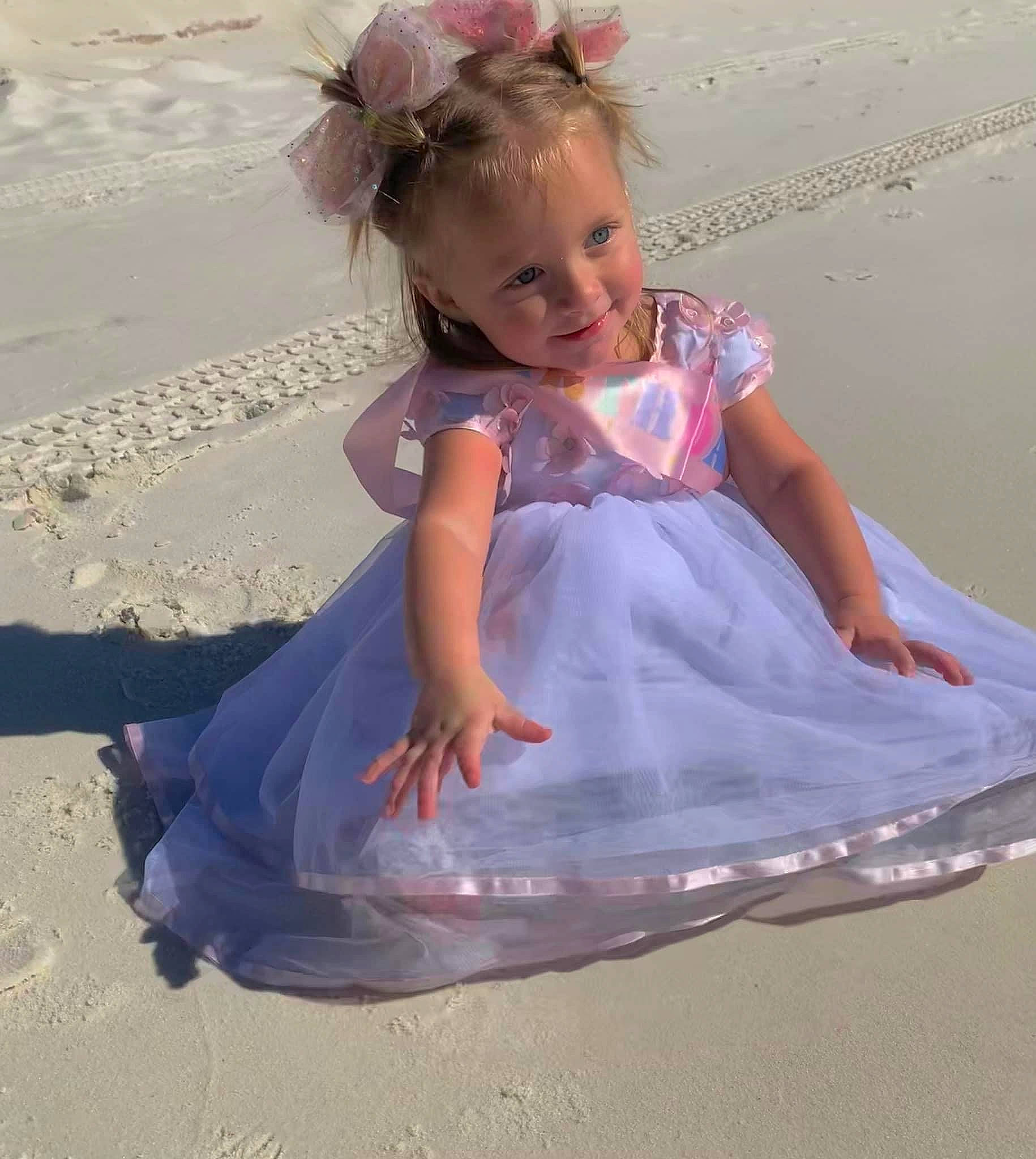 Indy is registered to the contest to win money with this photo: baby_toddler_clothing, barefoot, beach, bridal_accessory, child, dress, eye, fashion_accessory, fun, hair, hand, happy, head, human_body, leisure, person, pink, play, sitting, smile