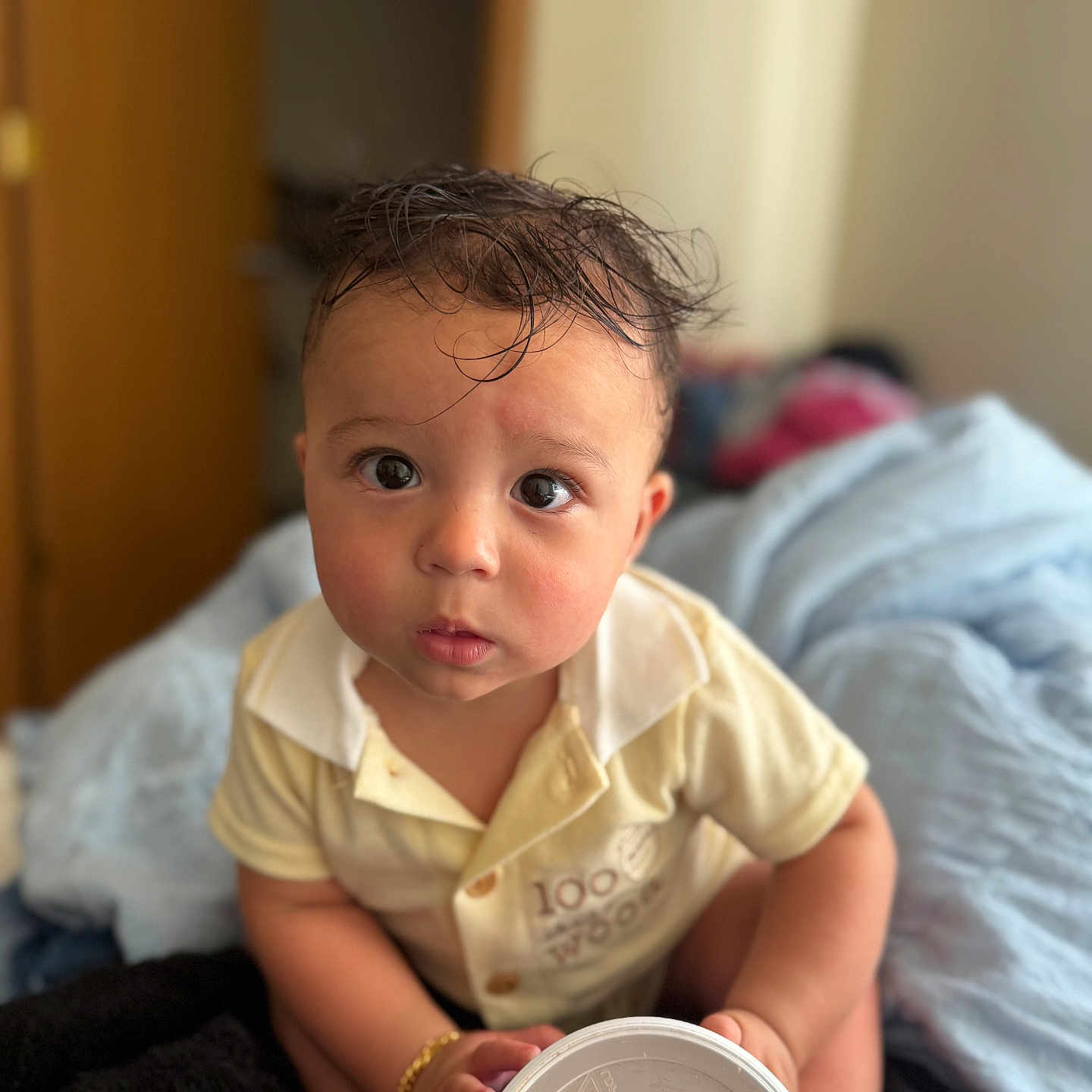 Azariah is registered to the contest to win money with this photo: baby, blanket, bracelet, child, clothing, container, curious, cute, expression, face, foot, hair, indoor, person, portrait, room, sitting, soft_light, yellow_shirt, young