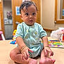 baby, child, infant, onesie, banana_pattern, bracelet, table, indoor, curious, sitting, toys, book, wooden_surface, portrait, cute, small_hands, small_feet, short_hair, expression, room