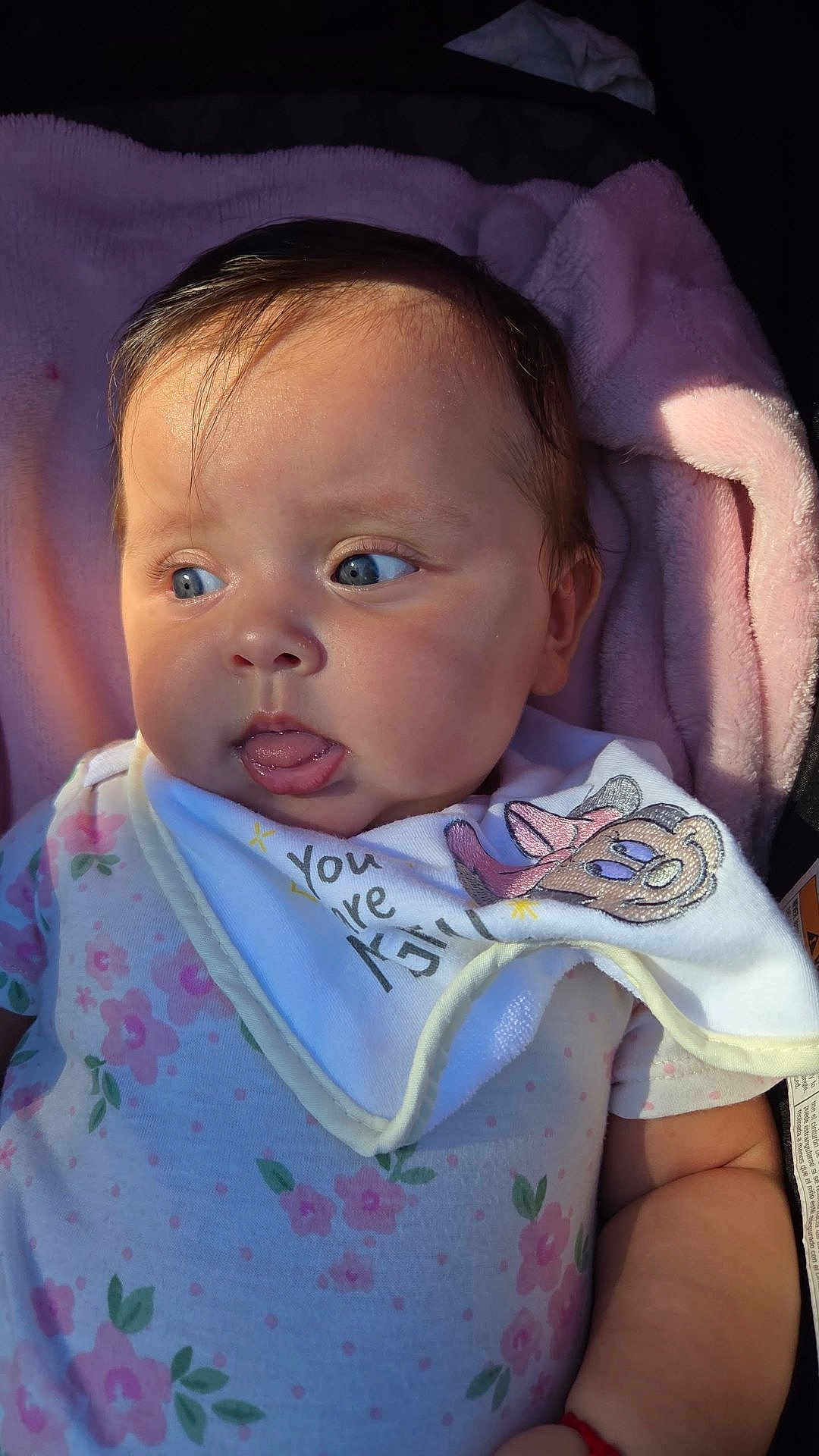 Mia Charlotte is registered to the contest to win money with this photo: baby, infant, child, blue_eyes, tongue_out, pink_blanket, floral_outfit, bib, cartoon_character, soft_light, closeup, cute, skin, face, expression, person, sleepwear, newborn, young_child, indoors