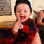 August joined the competition — help win amazing prizes! baby, infant, smiling, beanie_hat, plaid_onesie, red_and_black, hands_clasped, open_mouth, drooling, living_room, couch, coffee_table, wall_art, window_blinds, adult_arm, tattoo, hand_holding, happy, portrait, closeup