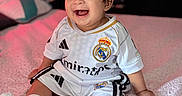 Endrick joined the competition — help win amazing prizes! baby, bed, blanket, child, clothing, cozy, cute, happy, home, indoor, infant, person, portrait, real_madrid, short_hair, sitting, smiling, soccer_uniform, soft_lighting, white_socks