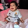 baby, bed, blanket, child, clothing, cozy, cute, happy, home, indoor, infant, person, portrait, real_madrid, short_hair, sitting, smiling, soccer_uniform, soft_lighting, white_socks