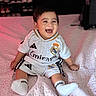baby, bed, blanket, child, clothing, cute, face, footwear, hair, happy, head, indoor, person, portrait, real_madrid, sitting, smiling, soccer_outfit, socks, young_child