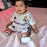 baby, bed, blanket, child, clothing, cute, face, happy, head, indoor, infant, person, portrait, real_madrid, sitting, smile, soccer_outfit, sportswear, white_socks, young_child