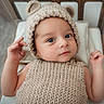 baby, infant, knitted_hat, bear_ears, knitted_sweater, cute, child, portrait, indoor, cushion, wooden_bed, neutral_colors, curious_expression, small_hands, closeup, soft_lighting, cozy, newborn, face, lying_down