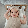 Shâyân is registered to the contest to win money with this photo: baby, infant, knitted_clothing, beige, bed, pillow, wooden_headboard, lying_down, cute, face, blue_eyes, soft_lighting, indoors, child, newborn, portrait, headwear, expression, sleeping_area, toddler