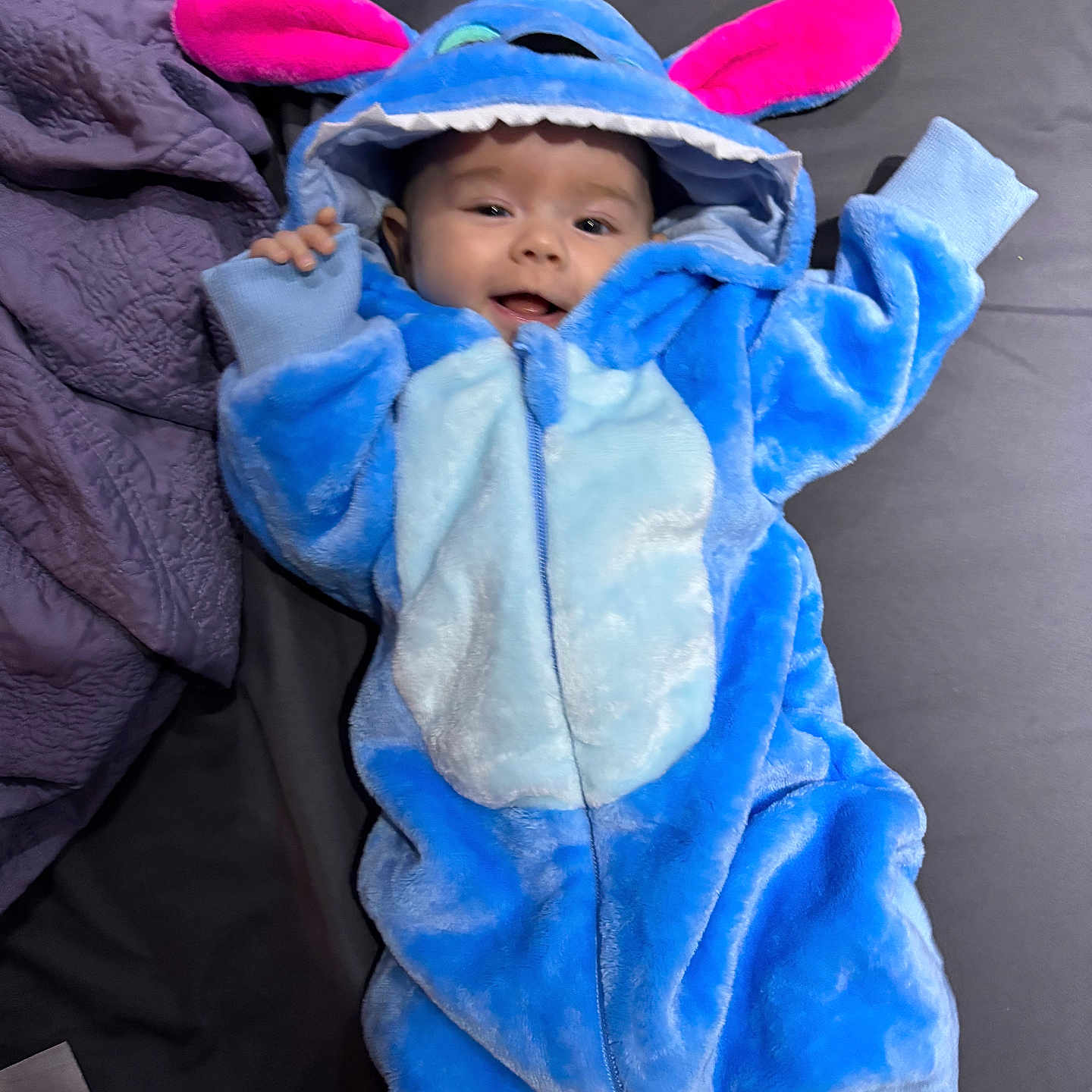 Billie Jean is registered to the contest to win money with this photo: baby, bed, blanket, blue, child, costume, cute, fabric, face, happy, hood, indoors, infant, lying_down, person, pink, plush, sleeve, small, smiling