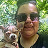 Cricket Lynn Greene is registered to the contest to win money with this photo: casual_clothing, chihuahua, close_up, daylight, dog, face, greenery, hand, happy, nature, necklace, outdoor, person, pet, portrait, shadow, short_hair, smile, sunglasses, sunlight