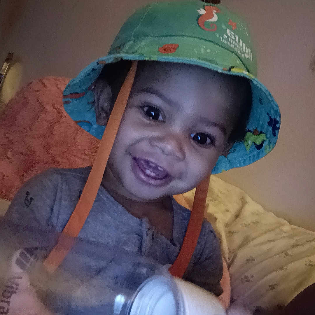 Zy'Aire is registered to the contest to win money with this photo: baby, bodypart, bonnet, cap, clothing, couch, cup, face, finger, furniture, hand, hardhat, hat, head, helmet, lamp, person, photography, portrait, sunhat