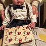 baby, child, infant, bow_tie, suspenders, gift, present, table, hands, tattoo, clothing, footwear, white_shoes, patterned_tablecloth, indoor, portrait, cute, wide_eyes, hat, person