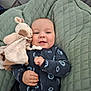 baby, infant, smiling, plush_toy, giraffe, quilted_cushion, clothing, onesie, happy, face, hand, soft_texture, indoor, cute, child, lying_down, comfort, cozy, portrait, person