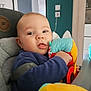 baby, child, plush_toy, high_chair, indoor, cozy, curious, seated, colorful, soft_toy, face, person, furniture, modern_decor, teal_wall, clothing, cute, infant, expression, home