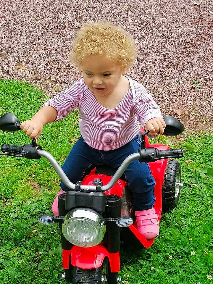 Naelya a rejoint le concours — aidez-le/la à gagner de superbes lots ! automotive_lighting, baby_products, baby_toddler_clothing, child, face, fun, gardening, grass, lawn, motor_vehicle, people_in_nature, person, plant, riding_toy, sitting, tire, toddler, toy, vehicle, wheel