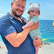 Mathèo a rejoint le concours — aidez-le/la à gagner de superbes lots ! baby, beach, casual_clothing, child, family, glasses, happy, hat, holding, man, ocean, outdoor, people, portrait, sand, sky, smile, sunny, vacation, water