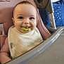 baby, high_chair, bib, food, messy, smile, child, indoor, feeding, face, person, happy, green_food, cute, infant, seat, pink, plastic, table, tongue