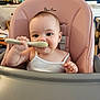 Sofia joined the competition — help win amazing prizes! baby, high_chair, spoon, infant, child, feeding, smile, face, person, indoor, furniture, pink, white_clothing, cute, expression, holding, home, sitting, kitchen, background
