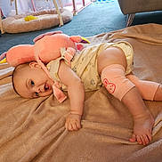 Sofia is registered to the contest to win money with this photo: baby, infant, plush_toy, blanket, carpet, indoor, soft_toy, cute, child, leg_warmers, clothing, foot, hand, person, relaxing, floor, home, comfort, playful, expression