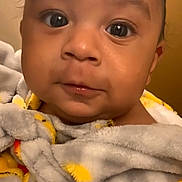 Kamaz is registered to the contest to win money with this photo: baby, close_up, blanket, cozy, cute, face, infant, indoors, looking_at_camera, portrait, wrapped, yellow, orange, soft, warm, child, young, expression, skin, head