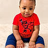 baby, child, portrait, sitting, smiling, spiderman, superhero, red_shirt, blue_pants, shoes, bracelet, curly_hair, face, eyes, indoors, rug, studio_photo, fashion, cute, front_view
