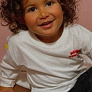 Assia a rejoint le concours — aidez-le/la à gagner de superbes lots ! toddler, child, smiling, curly_hair, red_bow, white_shirt, dark_pants, cushion, indoor, portrait, happy, cute, person, sitting, young_child, casual_clothing, face, skin, head, eyebrows