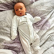 Ivar is registered to the contest to win money with this photo: baby, infant, onesie, bed, bedding, pattern, face, tongue_out, lying_down, cute, child, newborn, sleepwear, soft, bedroom, resting, young, person, playful, expression