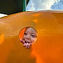 Carmello is registered to the contest to win money with this photo: child, playground, orange, hole, smiling, fingers, outdoor, sky, clouds, play, fun, happy, face, curious, daylight, structure, yellow, person, young, expression