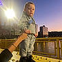toddler, child, person, grey_tracksuit, nike_logo, black_shoes, hand_holding, yellow_bridge, city_skyline, evening, streetlamp, river, reflection, urban, outdoor, railing, buildings, sunset, sky, casual_clothing