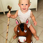 Tom participe au concours pour gagner de l'argent avec cette photo : toddler, child, indoor, toy, inflatable_horse, walking_stick, white_tank_top, floor_tiles, kitchen, barefoot, blond_hair, blue_eyes, smiling, play, fun, cute, person, baby, young_child, home