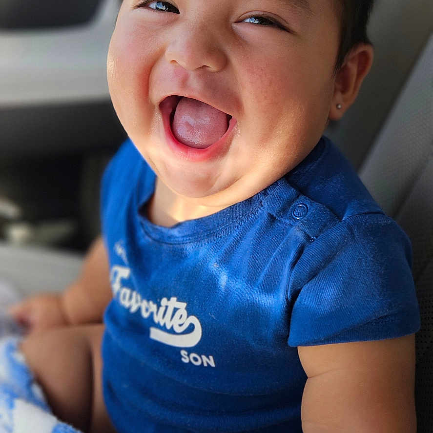 Gabriel joined the competition — help win amazing prizes! baby, child, toddler, smiling, laughing, portrait, face, indoor, car, vehicle, seated, blue_shirt, blanket, earring, happy, close_up, photography, passenger, joyful, family