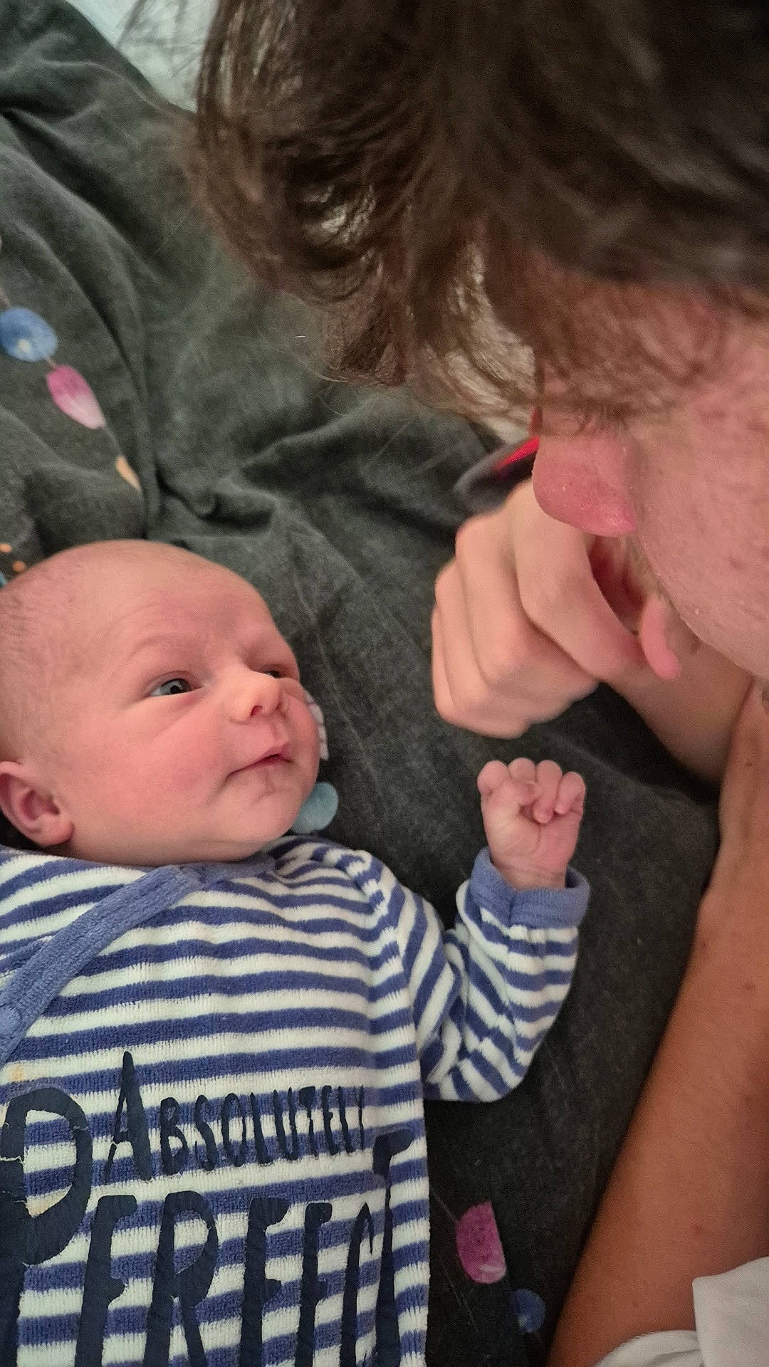 adult, baby, blanket, closeup, cuddle, curly_hair, expression, face, family, gaze, hand, indoor, interaction, love, newborn, onesie, person, portrait, skin, striped_clothing