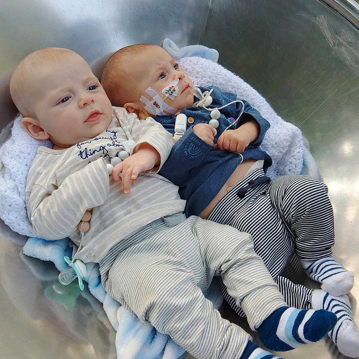 Jax And Jace is registered to the contest to win money with this photo: baby, blanket, bowl, child, clothing, cute, face, grass, hands, infant, lying_down, medical_tape, metal, outdoor, pacifier, peaceful, sensor, socks, striped_pants, two_children