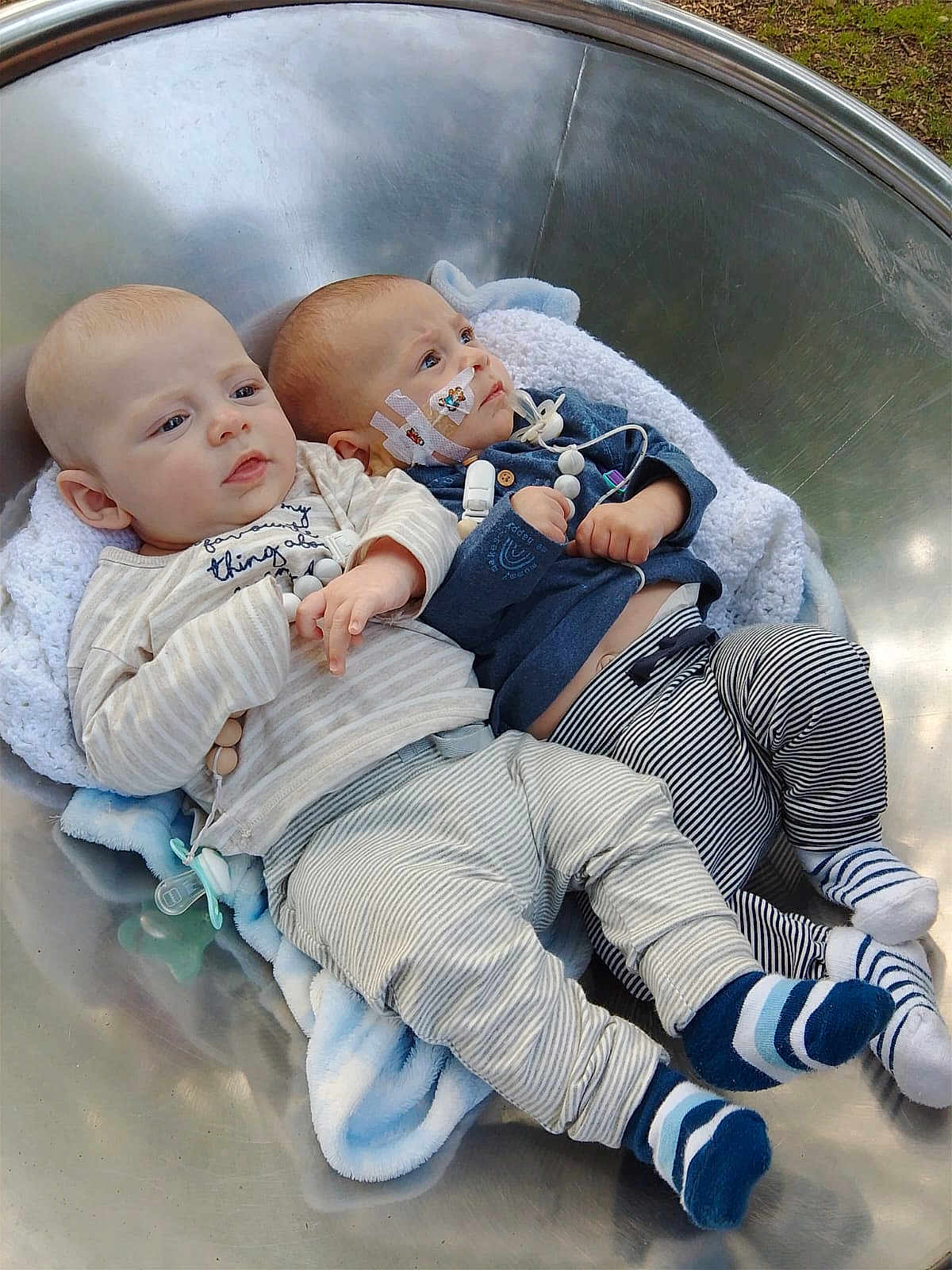 Jax And Jace is registered to the contest to win money with this photo: baby, infant, child, blanket, bowl, metal, clothing, striped_pants, socks, pacifier, medical_tape, sensor, outdoor, grass, cute, lying_down, two_children, face, hands, peaceful