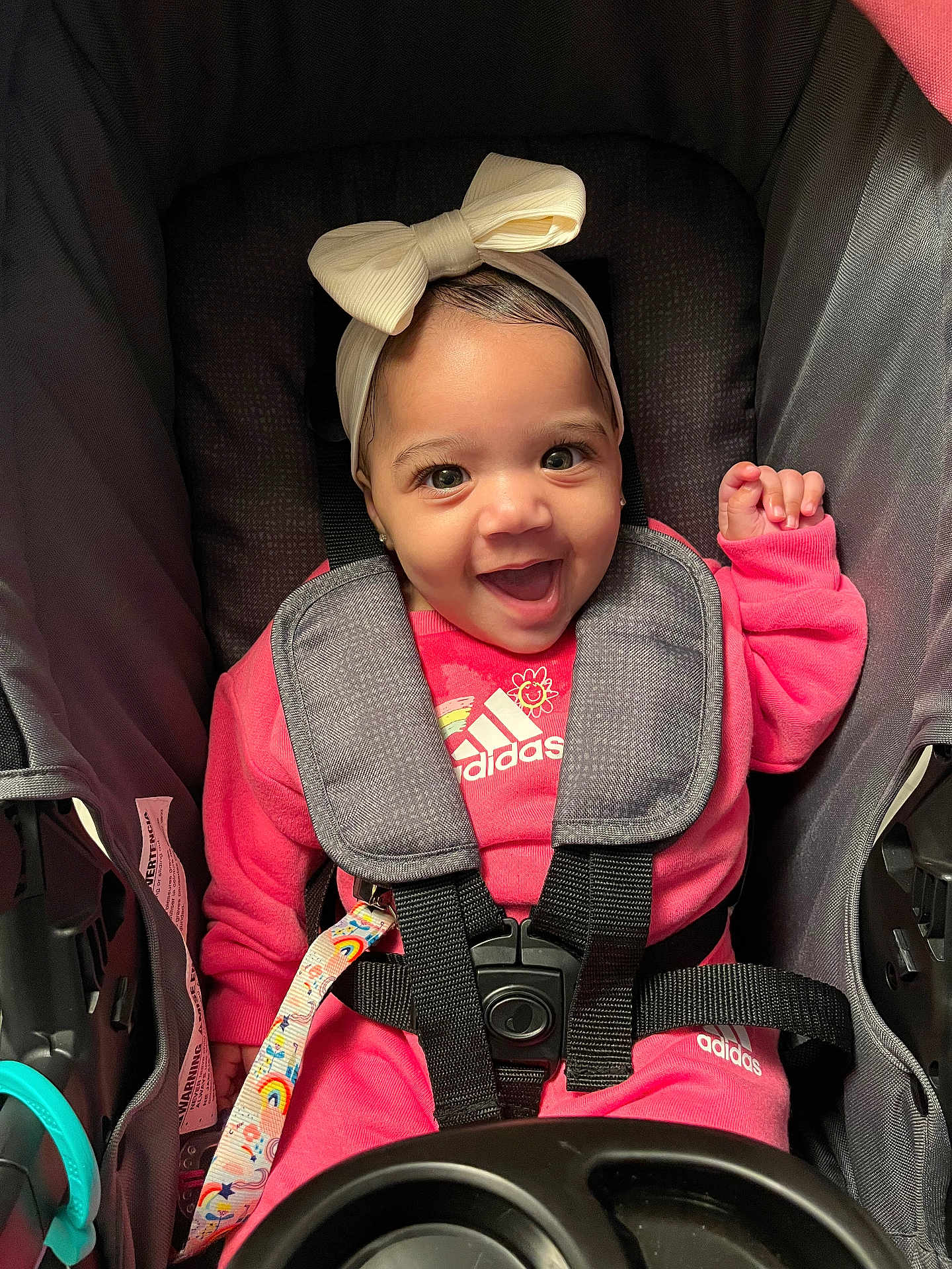 Amilya is registered to the contest to win money with this photo: baby, child, smiling, pink_clothing, headband, bow, stroller, seatbelt, adidas, happy, infant, cute, portrait, sitting, eyes, face, clothing, baby_girl, indoor, baby_accessory