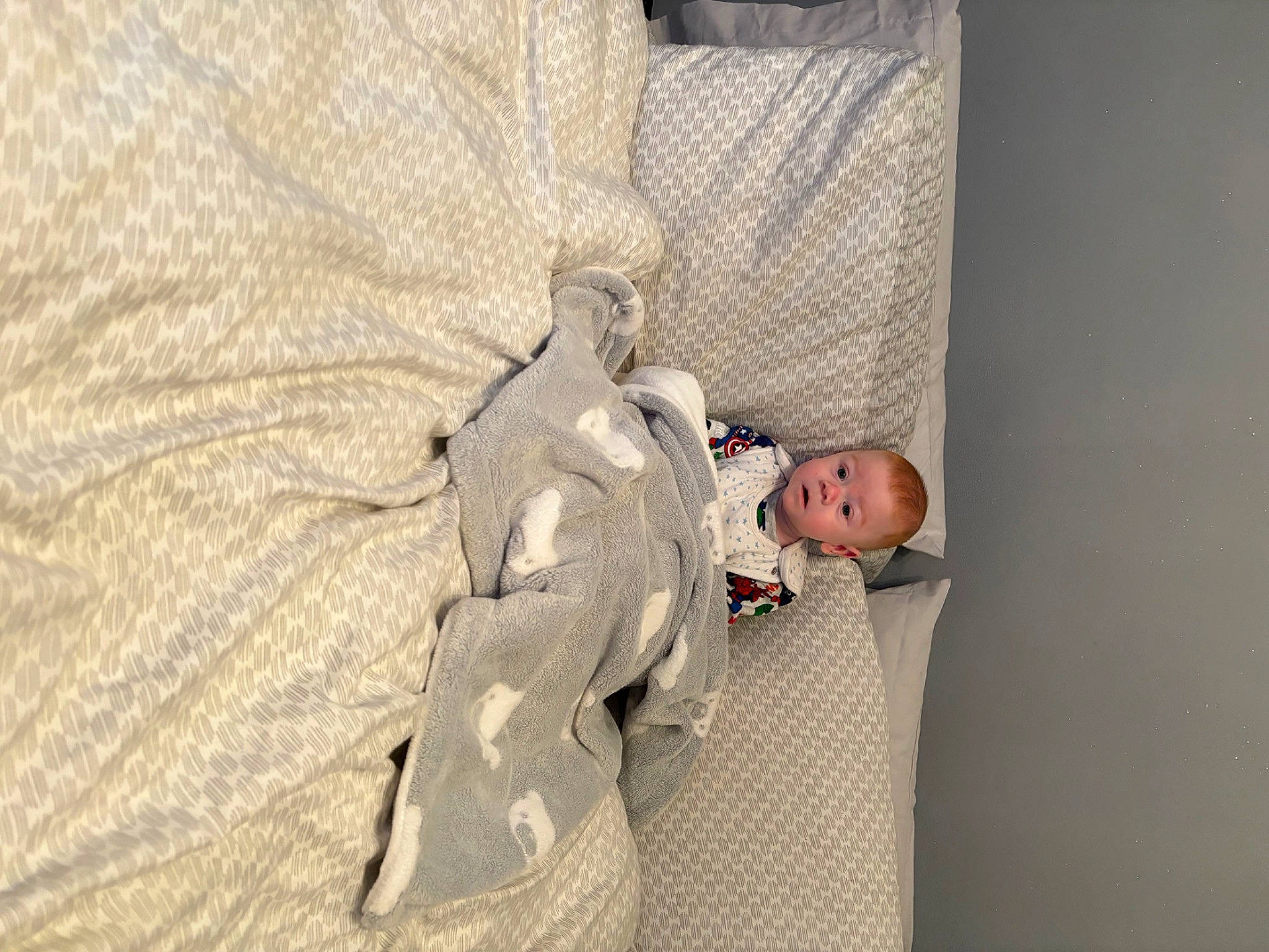 Teddy is registered to the contest to win money with this photo: baby, baby_products, baby_toddler_clothing, bedding, bedtime, child, comfort, flooring, gesture, infant_bed, knee, linens, person, plaster, room, sitting, sleep, sleeve, surprise, throw_pillow