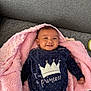 baby, infant, blanket, pink_blanket, sofa, couch, smile, crown, onesie, clothing, portrait, lying_down, cheeks, head, hair, eyes, hand, fabric, polka_dot, indoor