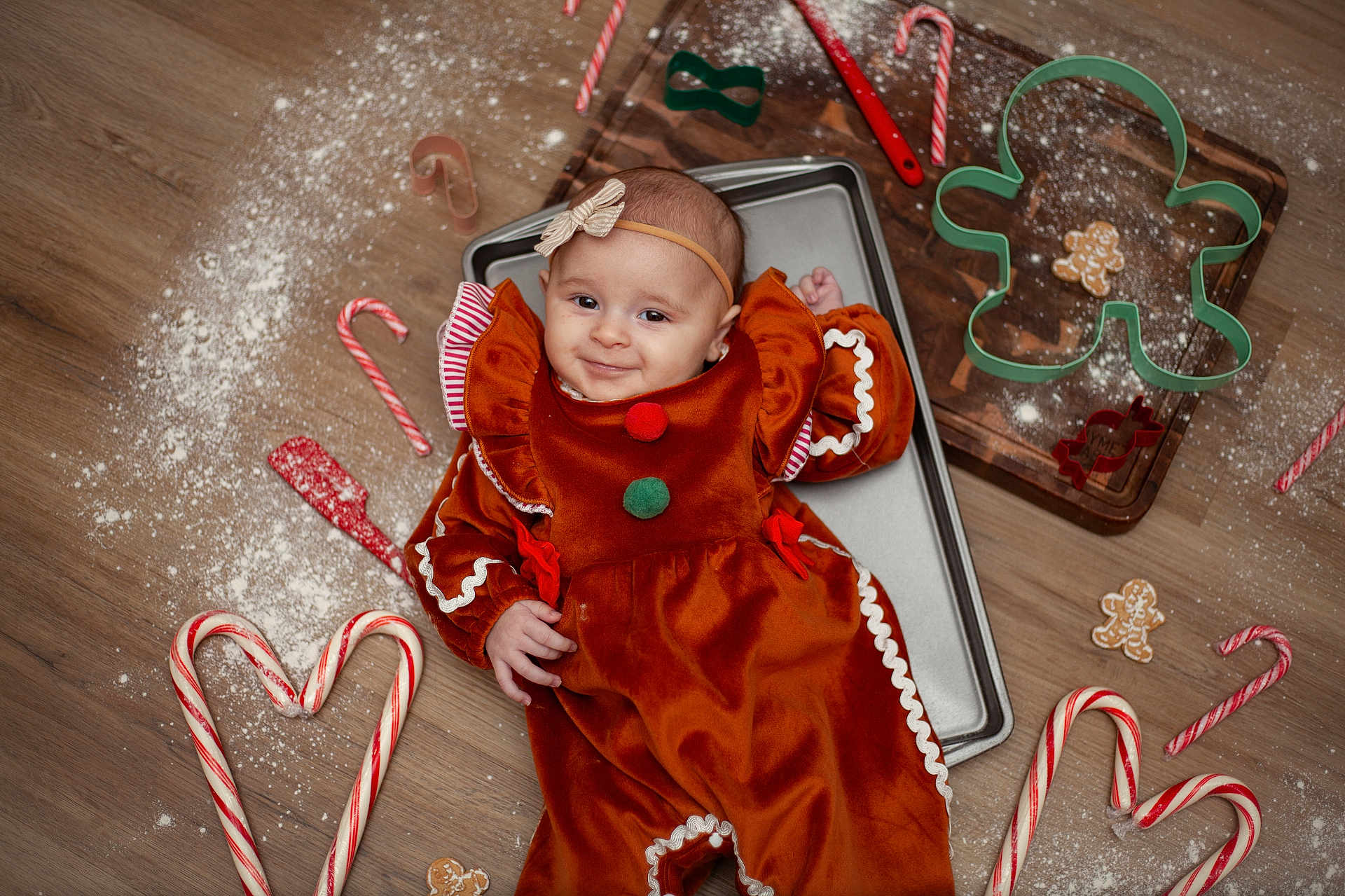 Sofia joined the competition — help win amazing prizes! baby, child, gingerbread_costume, candy_cane, cookie_cutter, flour, baking_tray, wooden_floor, holiday, christmas, smile, red, green, headband, cute, festive, playful, indoors, person, portrait