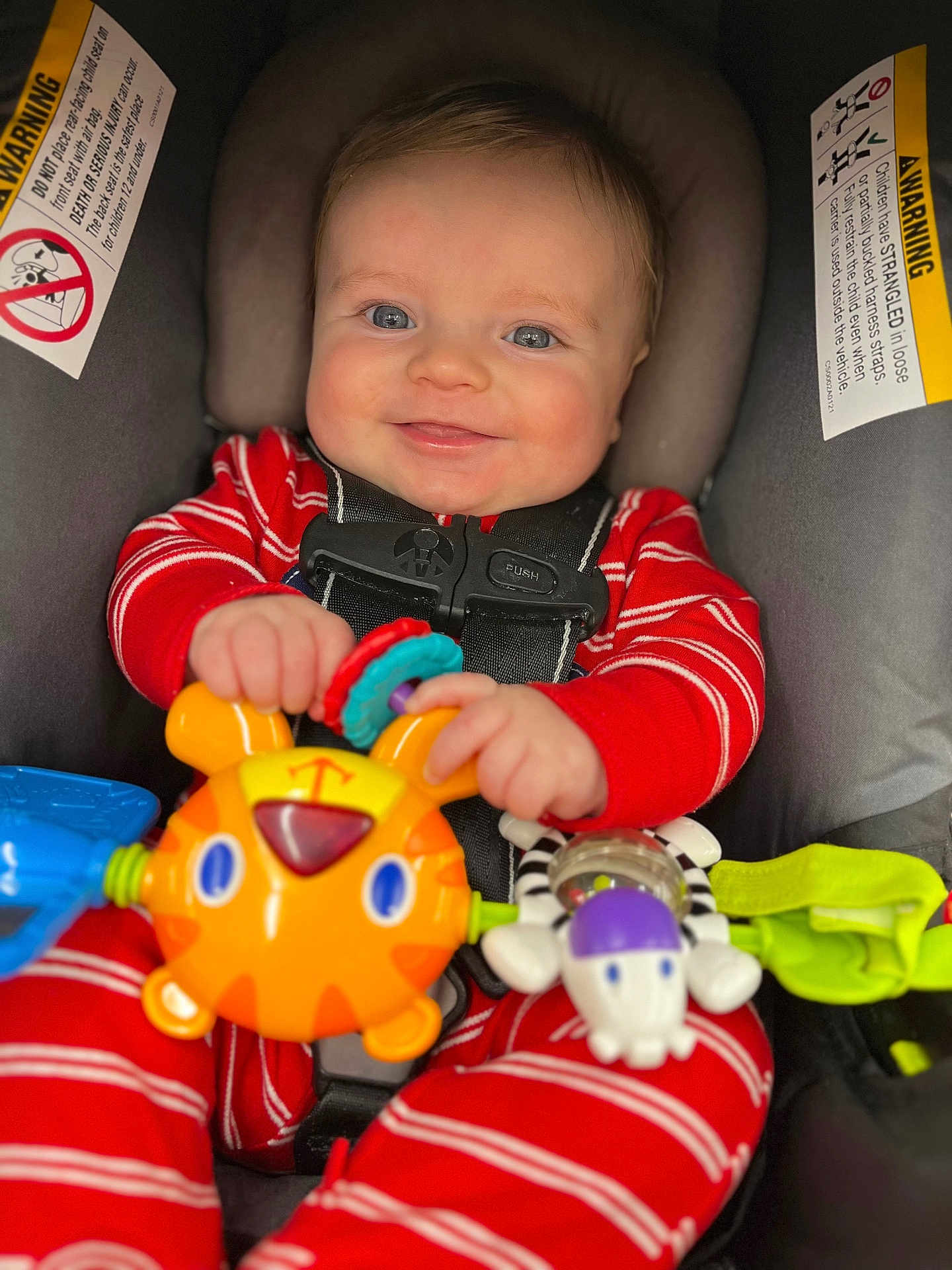 Maverick joined the competition — help win amazing prizes! baby, blue_eyes, car_seat, child, closeup, colorful, comfort, cute, face, hands, happy, indoor, infant, playful, red_clothing, safety, seatbelt, smile, striped_pajamas, toy
