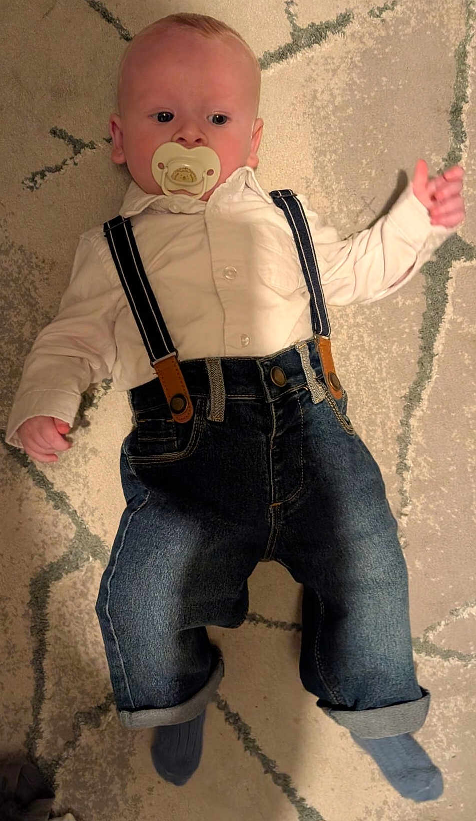 Reece is registered to the contest to win money with this photo: baby, carpet, casual, child, clothing, cute, denim, floor, home, indoor, infant, jeans, laying_down, pacifier, person, portrait, shirt, sock, suspenders, young_child