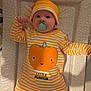baby, infant, pacifier, striped_clothing, yellow, white, pumpkin_design, hat, polka_dot, changing_pad, lying_down, cute, child, indoors, soft_lighting, portrait, one_person, smiling_pumpkin, baby_clothes, headwear