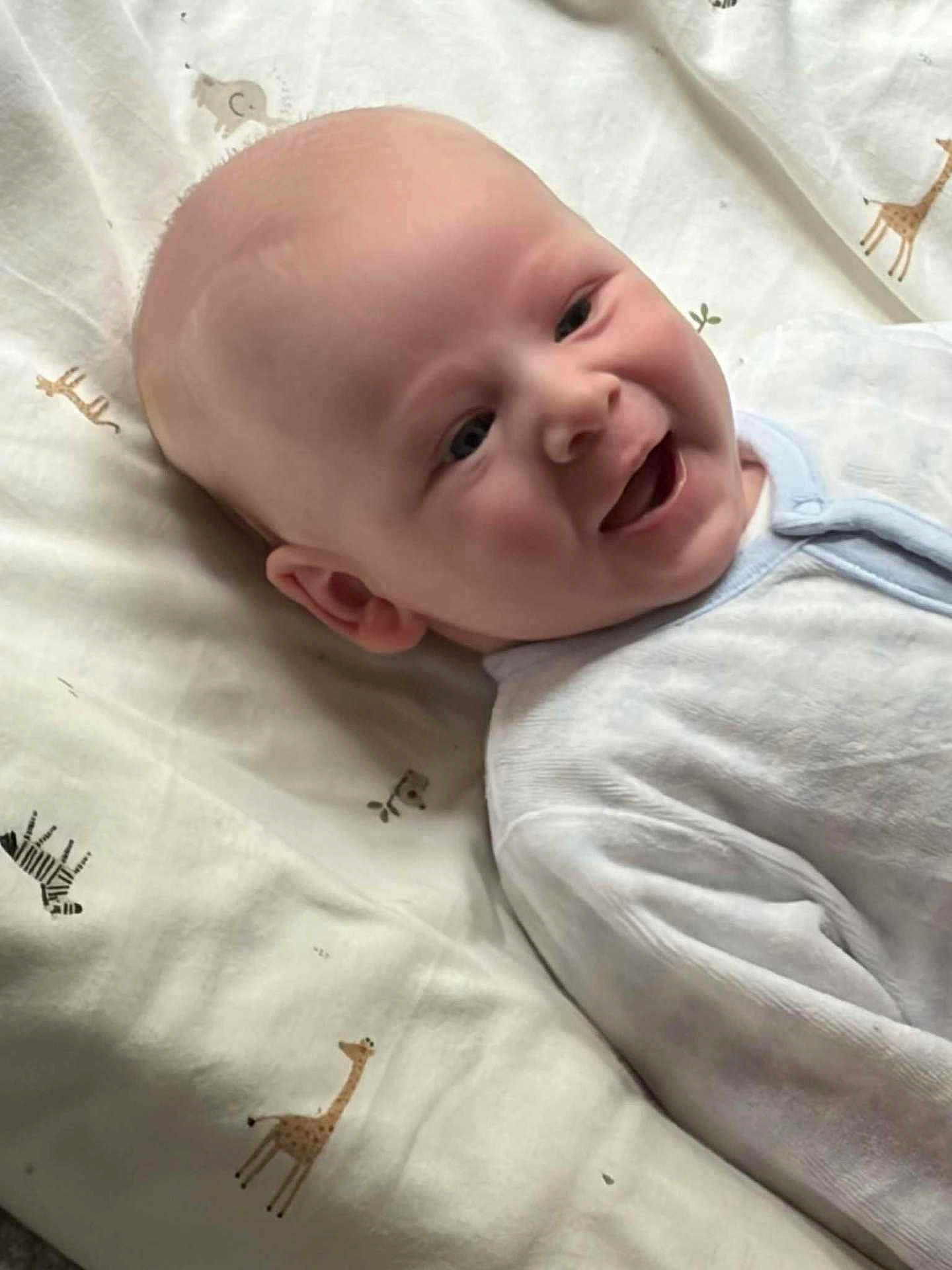 Reece joined the competition — help win amazing prizes! baby, smiling, infant, lying_down, blanket, animal_print, giraffe, zebra, clothing, white_outfit, happy, cute, face, head, person, child, soft_lighting, indoor, closeup, portrait