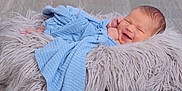 Terry is registered to the contest to win money with this photo: newborn, baby, smile, blue_cloth, fluffy_cushion, wooden_floor, sleeping, wrapped, cozy, infant, cute, soft_texture, happy, resting, portrait, child, indoors, peaceful, fresh, small