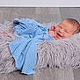 newborn, baby, smile, blue_cloth, fluffy_cushion, wooden_floor, sleeping, wrapped, cozy, infant, cute, soft_texture, happy, resting, portrait, child, indoors, peaceful, fresh, small