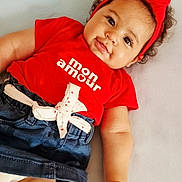 Aria participe au concours pour gagner de l'argent avec cette photo : baby, infant, child, curly_hair, red_headband, red_shirt, denim_skirt, white_bow, cute, smiling, lying_down, soft_light, portrait, indoor, adorable, fashion, clothing, face, hand, skin