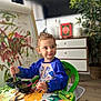 child, toddler, painting, paintbrush, smock, art, easel, colorful, table, indoor, green_chair, drawing, expression, curly_hair, playful, creative, art_supplies, face, person, home
