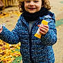 child, curly_hair, blue_jacket, bubble_wand, bubble, outdoor, autumn, leaves, path, smiling, happy, scarf, playful, person, fall, young_child, nature, jacket, toy, daylight